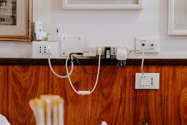 a wall mounted white power strip with and multiple electrical outlets with lots of devices plugged into them