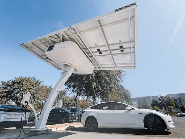  a white Tesla plugged into a solar-powered EV charging station