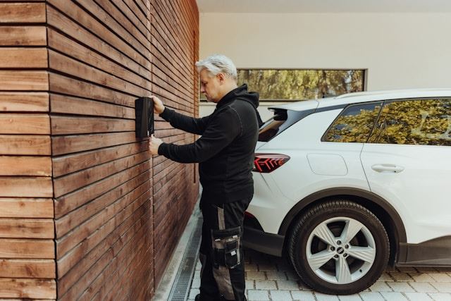  a man dressed in black installing an EV home charger next to a white car