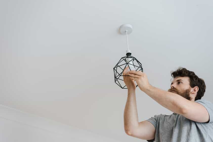 a close up of a man switching a light bulb on a ceiling lamp