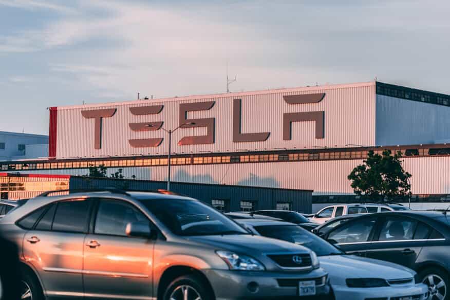 cars parked in a parking lot in front of a Tesla company building