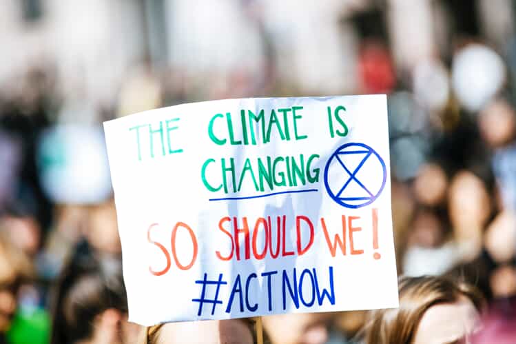  a banner being held up in a crowd that says the climate is changing, we should too. Act now