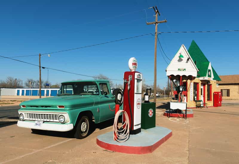  an old mint green car at a gas pump on a sunny day